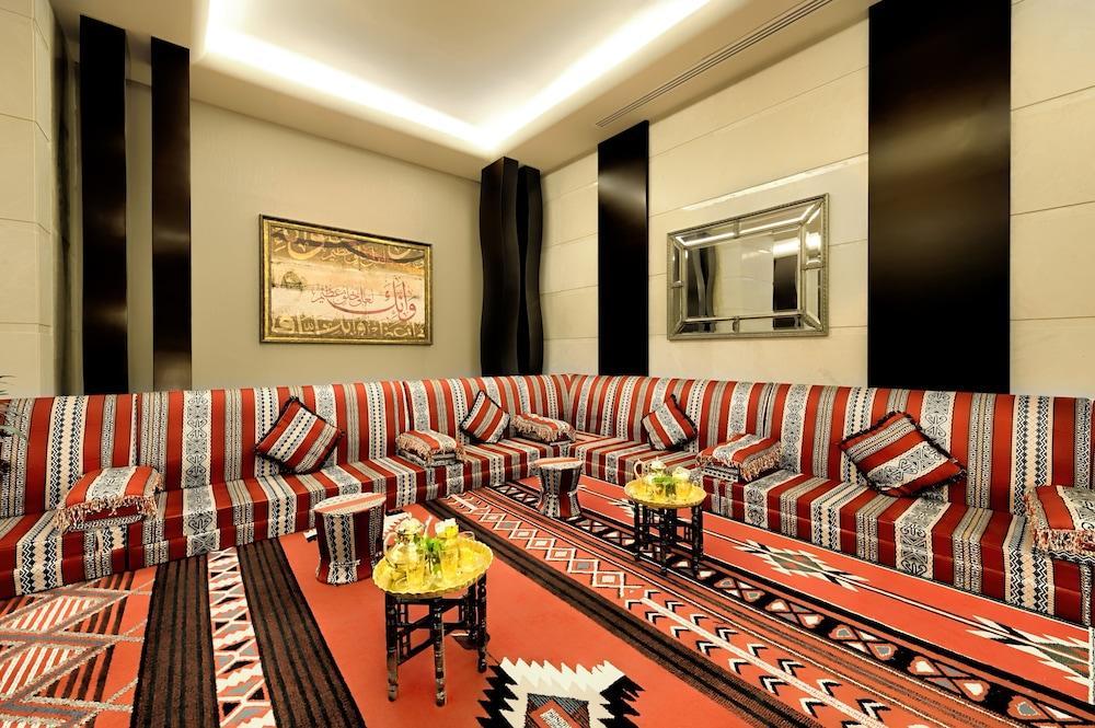 Al Ghufran Safwah Hotel Makkah Mekka Eksteriør billede The photo depicts a spacious and elegantly designed living room. The seating area features a large, L-shaped couch adorned with colorful cushions, primarily in red, black, and white patterns. The walls are decorated with sleek, modern finishes, and l