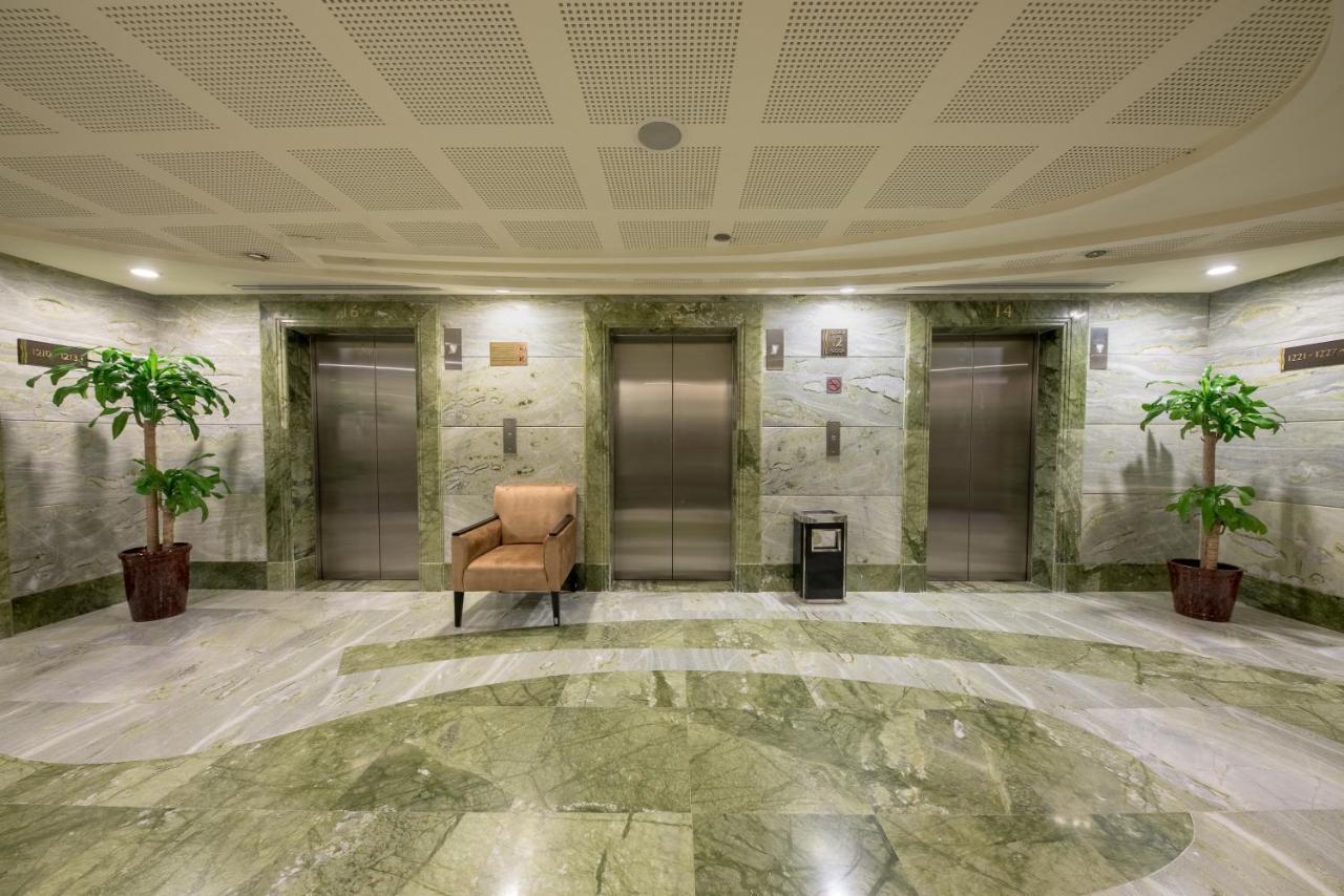 Al Ghufran Safwah Hotel Makkah Mekka Eksteriør billede The image shows a lobby area with a modern design. It features several elevator doors arranged in a row. The walls are made of a light-colored marble with a green hue, and the flooring is also marble, creating a cohesive and elegant look. On either s