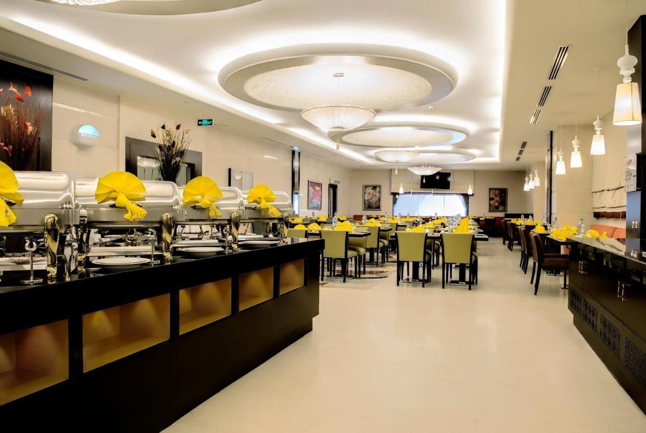 Al Ghufran Safwah Hotel Makkah Mekka Eksteriør billede The photo depicts a modern restaurant interior. There is a wide open space with a contemporary design. On one side, there are several buffet-style food trays, likely for self-service dining. The tables are set with yellow napkins, and the seating app