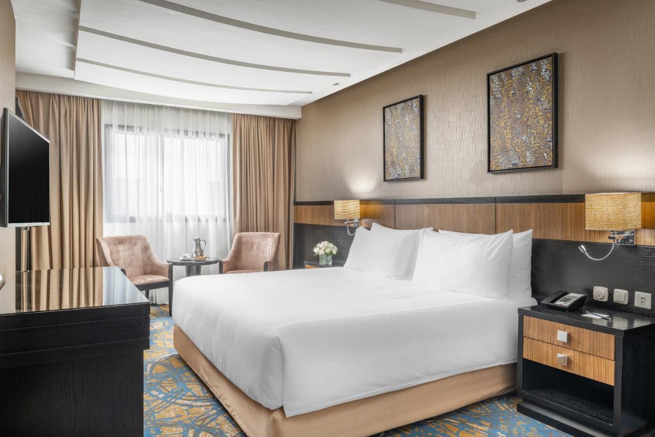 Al Ghufran Safwah Hotel Makkah Mekka Eksteriør billede The photo shows a modern hotel room featuring a spacious layout. In the center, there is a large bed with white linens. To the side, there are two upholstered chairs and a small table, creating a cozy sitting area. The room is decorated with stylish 
