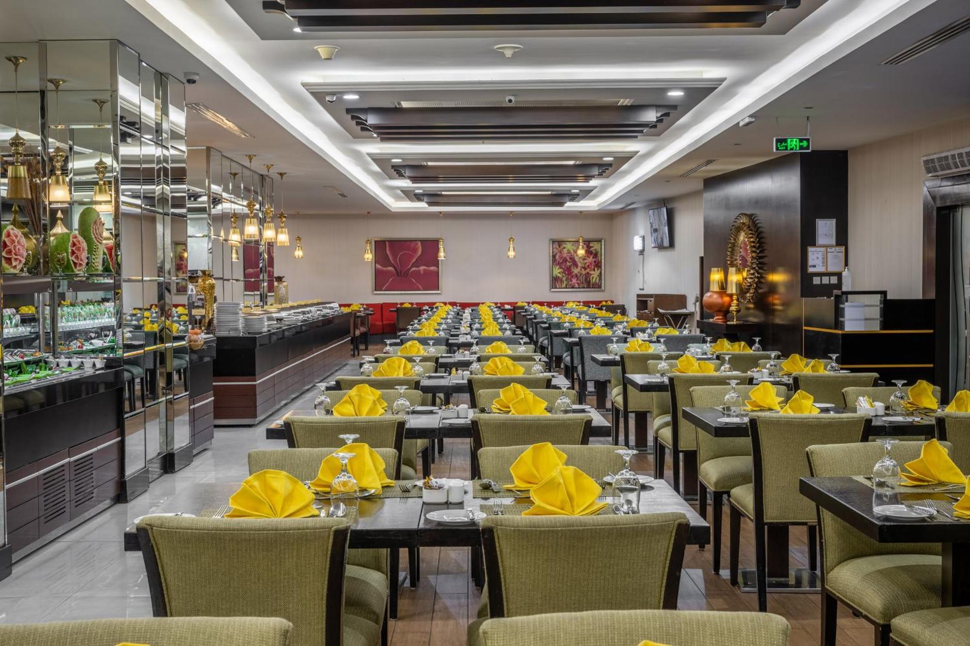 Al Ghufran Safwah Hotel Makkah Mekka Eksteriør billede The photo shows the interior of a restaurant. The dining area features multiple rows of tables, each set with yellow napkins and glassware. The tables are covered with dark-colored tablecloths and are surrounded by green upholstered chairs. The resta