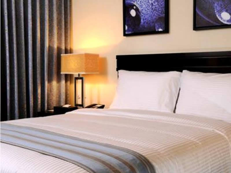 Al Ghufran Safwah Hotel Makkah Mekka Eksteriør billede The photo shows a cozy hotel room with a neatly made bed that has a white comforter featuring subtle stripes. There are two fluffy white pillows on the bed. On the wall above the bed, there are two framed artworks with abstract designs in blue and bl